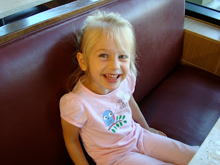 Young girl wearing pink with pony tail sitting in booth smiling