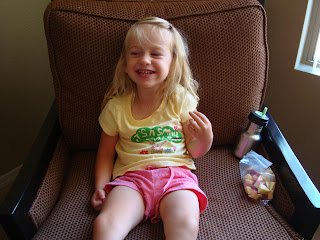 Young girl sitting in brown chair smiling and eating snack