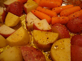 Close up of red and yukon gold potatoes, baby carrots with oil, salt, pepper and ginger in foil lined pan