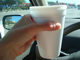 Hand holding up foam cup of coffee in car