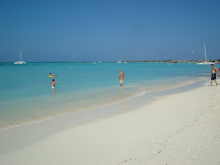 White sandy beach with people and boats in water