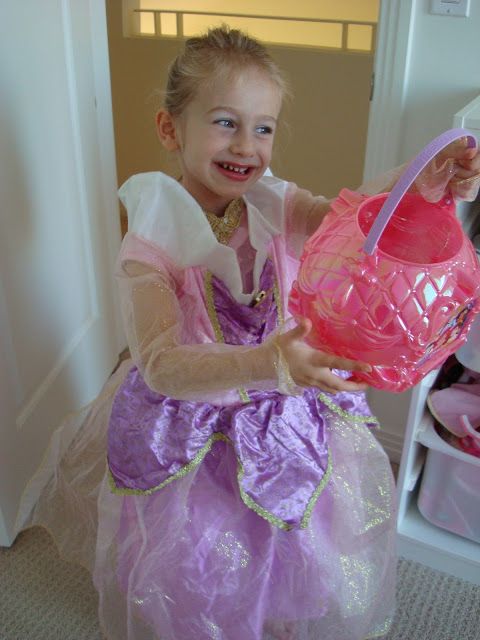 Young girl dressed in halloween costume holding up halloween bucket and smiling