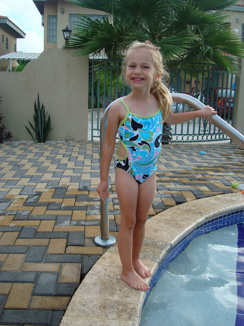 Young girl in swimsuit standing by pool holding onto railing