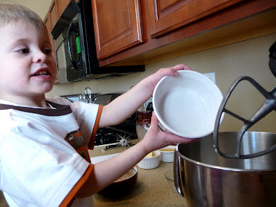 Little boy adding ingredients to a stand mixer. 