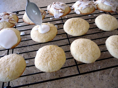 Lemon almond cookies on a cooling rack, being glazed. 
