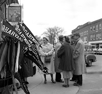 A photograph of people outside the Hanover Inn, looking at a display of Harvard pennants.