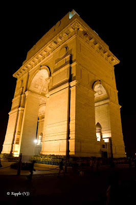 A Late Evening Glance at India Gate with my Travelling Camera: Posted by VJ SHARAM at www.travellingcamera.com : The India Gate is one of the largest war memorials in India. Situated in the heart of New Delhi, India Gate was designed by Sir Edwin Lutyens. It is a prominent landmark in Delhi and commemorates the members of the erstwhile British Indian Army who lost their lives fighting for the Indian Empire in World War I and the Afghan Wars. Originally, a Statue of King George V had stood under the now-vacant canopy in front of the India Gate, and was removed to Coronation Park with other statues. Following India's independence, India Gate became the site of the Indian Army's Tomb of the Unknown Soldier, known as the Amar Jawan Jyoti.(Courtesy: wikipedia)Standing Tall against the SkyIndia Gate looks amazing in the evening with well placed lights around it... Many Families in Delhi comes to India Gate in the evening and some of them come with all the stuff for dinner... There are luh green lawns around India Gate where one can sit and enjoy with family and friends...Lonely and Majestic..All these photographs have been shot without Tripod so they are blurry, which is more clear in the photograph above... Once I had seen an exhibition by Anindo Ghosh @ IHC Delhi and he had some brilliant shots of India gate, serial lights around it and their reflection in water ponds on its sides... All of them were stunning shots of INDIA GATE...A Permanent Flame...I usually visit India Gate with friends in the evening and take our Dinner at Andhra Bhavan which is on the circular road around India Gate... we need to take the car on Ashoka Road and then a cut... Food at Andhra Bhavan is good and they serve Thali @ 80 Rs for one person.. Its Veg Thali with unlimited service of Rice, Roti, Number of dishes... Few things like Curd, Papad, sweet-dish is served only once... Non-Veg is available but we didn't like it.. So wehenever we go to Andhra Bhavan for Dinner, we only take Veg Thalis... In Lunch time Puri is served instead of Rotis...Secure 24 * 7..Security of INDIA GATE is taken care by Army and there is some restricted area near to actual Gate where nobody can go... There is circular iron-chain around main gate which defines the boundary for normal civilians... and Security people look great in their unique attire with nice boots and powerful guns...Every Night Hundreds Celebrate their Indian Origin...Normally people visit the pace but hit season is summers and monsoons... Of-course, one can find huge crowd at INDIA GATE everytime but yes evenings are more crowded... In the evenings, there are lot many eating options around it which starts from Chana-Jor-Garam, Bhel-Puri, various brands of Ice-Creams with different options, Pani-Puri, Chats and what not... Reaching out for the Sky... An Image of India... Day shots of India Gate from moving Car when we were heading towards India Gate from Rashtrapati Bhavan..Names Engraved in the Heart of India...A Moment to Reflect....The More I See the World, the Closer I Feel to India.... 