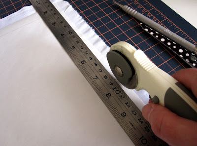 A rotary cutter, cutting along the edge of a metal ruler on a piece of white paper and fabric.