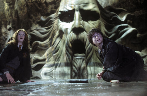 Gina Wesley e Harry Potter estão assustados e sentados no chão liso de uma câmara ampla cujas paredes são em pedra, como se esculpida uma caverna no subsolo. Há um enorme rosto esculpido de um velho barbudo de longos cabelos espalhados para o alto e para os lados localizado no centro da cena.
