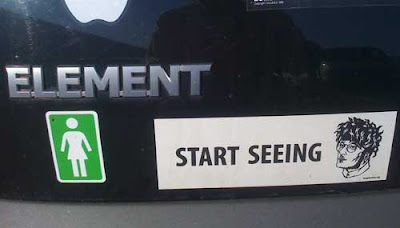Black and white bumpersticker on a black car. It says START SEEING followed by a drawing of a bespectacled man with a funny hairdo