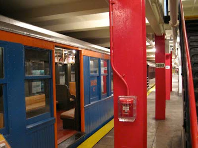 Red and blue wooden train car next to a subway platform