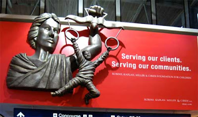 Red billboard with metal bas relief sculpture attached of Lady Justice holding her scales, but instead of weights there are round rings attached and a boy is dangling from the rings