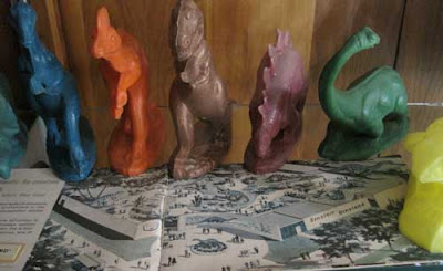 Multicolored wax dinosaur figures standing on a brochure showing a map of the Dinoland grounds