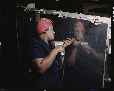 African American woman in a blue jumpsuit and red headscarf riveting a reflective metal panel