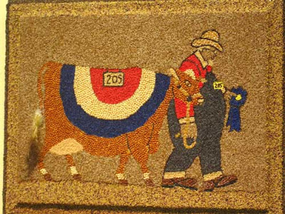 Oversized cow with a red white and blue blanket, being led by an elderly farmer in overalls