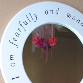 Edge of circular mirror with cutoff text and a reflection of a pink and purple flower chandelier