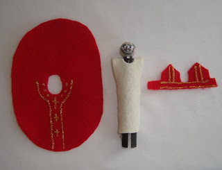 Red robe felt cutout and red deacon's cap cutout next to peg doll