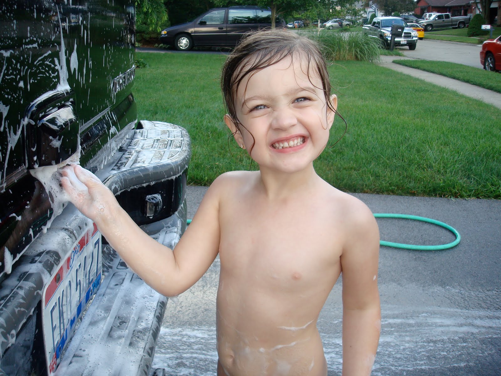 Young Preschool Girl Washing Car On Driveway In Front 