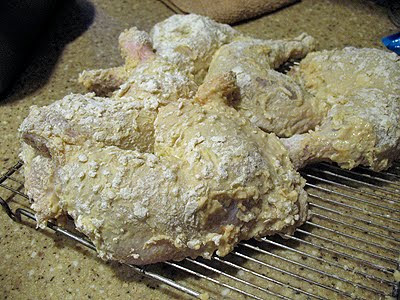 A photo of raw chicken coated an resting on a wire rack ready to be fried.