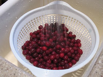 Cherries in a white colander being rinsed under water.