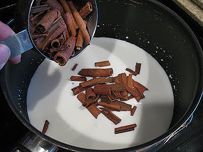 A close up photo of cinnamon sticks being added into the milk and cream in a saucepan.