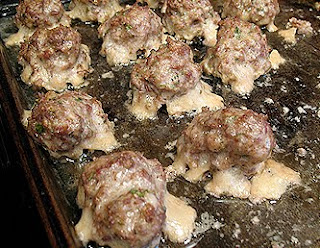 A close up photo of baked meatballs resting on a baking sheet.