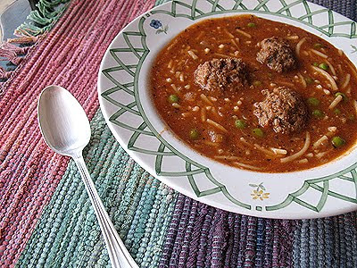 A close up photo of a bowl of Amanda\'s meatball soup with a spoon resting on the side.