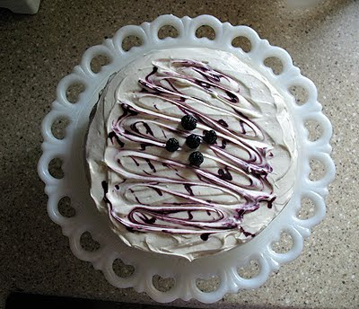 An overhead photo of a vanilla bean mulberry cake on a white cake stand topped with fresh mulberries.