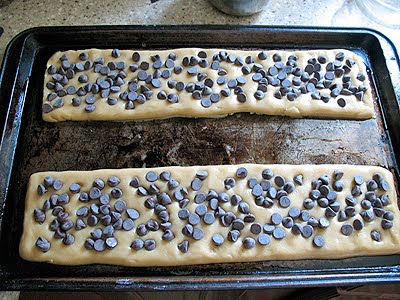 Cookie bar dough spread in two long portions onto a baking sheet with chocolate chips on top.