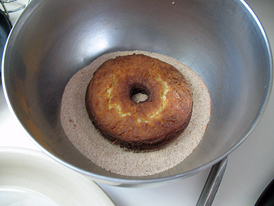 A photo of a doughnut resting on the cinnamon sugar mixture in a bowl.
